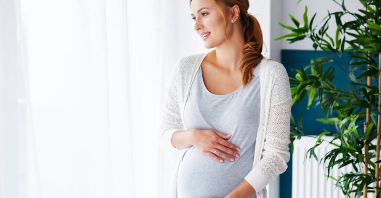 Cheerful pregnant woman looking through window