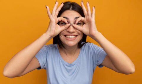 smiling-pretty-brunette-caucasian-girl-looks-camera-through-fingers-orange